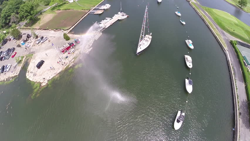 A firehose blesses a passing yacht at the annual Blessing of the Fleet celebration in Southport. 1080p aerial footage.