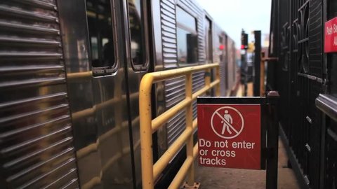 A train pulls out of a station in New York City next to a sign warning travellers to not enter or cross the tracks.