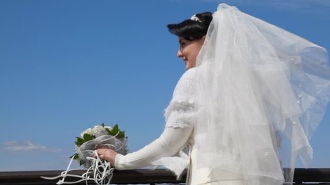 bride with bouquet on observation deck against blue sky 