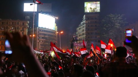 View from the ground as protestors chant, wave flags, and take cell phone pictures at a large nighttime rally in Tahrir Square in Cairo, Egypt.