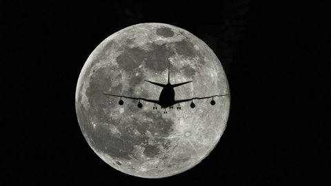 Plane silhouette against a full moon in the sky, airplane flying by the moon