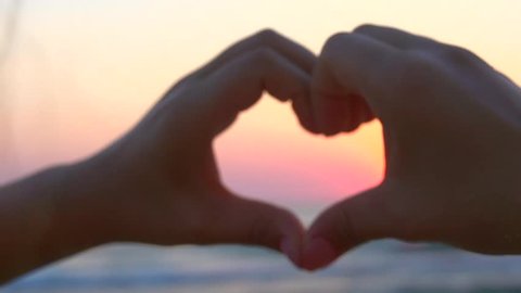 Beauty girl making heart with her hands over sea background. Happy young woman. Silhouette hand in heart shape with sunset inside. Vacation concept. Summer holidays. Tourism. Slow motion 240 fps 1080p