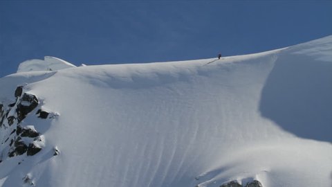 A freestyle skier charges down a beautiful snow covered mountain and triggers a little avalanche