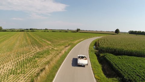 Friends having fun driving a vintage car in a country road, aerial view
