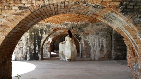 Black woman in a 1960's era bridal gown walks under the brick arches of an old fort built in the 1850's. Stock Video