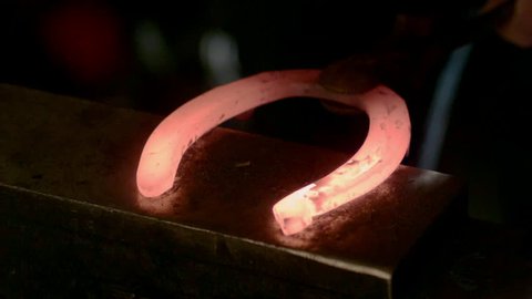 Close up on a red hot horseshoe as it's hit by a hammer.