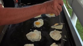 Cook flipping eggs over on hot grill for breakfast. Cooking eggs on cast iron camping grill outside. Outdoor breakfast picnic white and yellow eggs. 4K video.