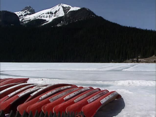 Lake Louise in Rocky Mountains scenery, early spring. Canoes on the bank of  frozen glacial lake + pan Chateau Lake Louise, Banff National Park, Canada.