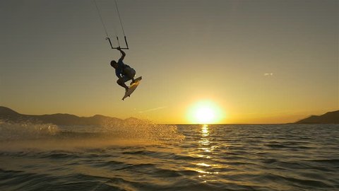 SLOW MOTION: Kiteboarder jumping at golden sunset