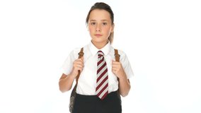 Young schoolgirl standing watching and waiting looking expectantly off to the side while clutching the straps of her backpack, on white