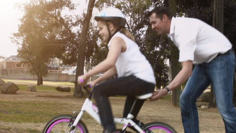 Father teaching daughter to ride her pink bike, steadicam shot. 