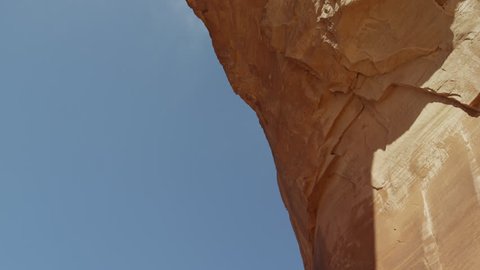 Wide tracking shot of man swinging from arch on rope / Corona Arch, Moab, Utah, United States