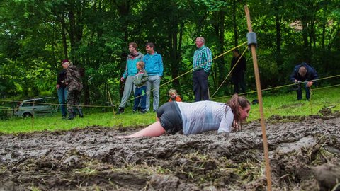 CELJE, SLOVENIA - MAY 2014: Gladiator games with obstacles while running on track. Woman crawling through mud as part of obstacle course