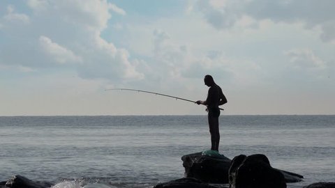Fisherman fishing standing on rock by sea 