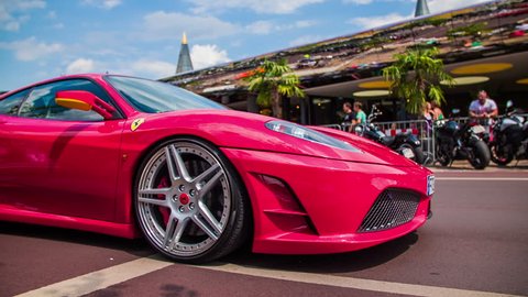 VELDEN, AUSTRIA - JUNE 2014: Street show supercars. Very expensive cars driving through town. Red Ferrari in slow motion low angle passing by