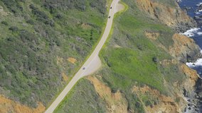 Aerial view of car travelling Californian coast along the Big Sur. Cliffs overlooking the blue Pacific ocean.