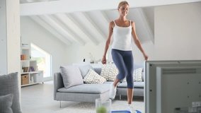 Young woman doing fitness exercises in front of TV 