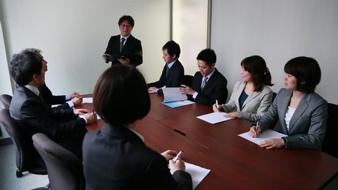 Japanese business people having a meeting around a wooden desk in a modern meeting room
