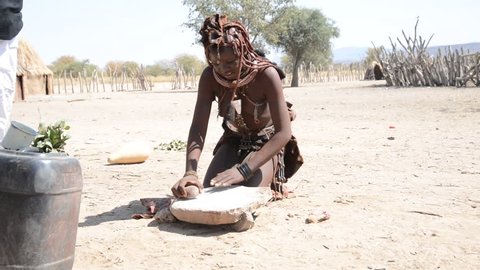 Namibia 08/24/2014: An Himba girl preparing the flour with stones. Himba, one of the oldest namibian tribes, live in his tradition not conforming to the new world rules and comfort..