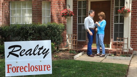 A man tries to console his wife who is distressed over the foreclosure sign in the front yard.