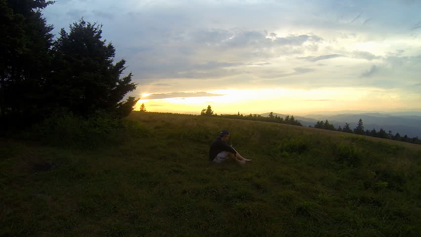 A young man sits on a mountain top texting at sunrise surrounded by beautiful scenery