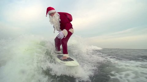Man in Santa Claus costume with gift bag freestyling on wake surf touching water