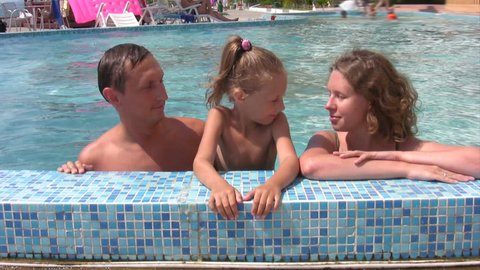 family of three persons talks in swimming pool outdoor 