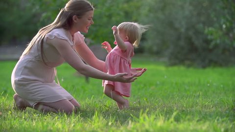Adorable toddler hardly keeping balance in her first steps to mother