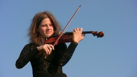 portrait of young woman plays violin against blue sky  