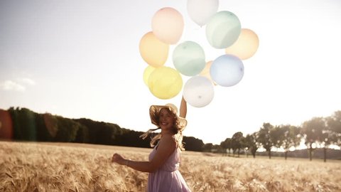 Girl running through wheat field holding balloons