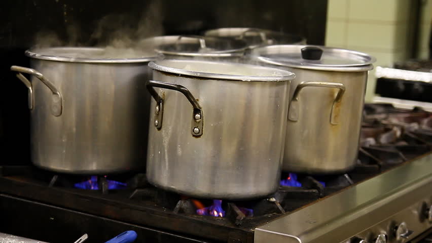 Pots cook on a stove in an industrial kitchen.