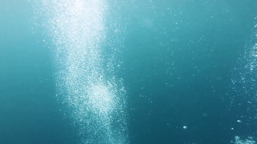 Diving up along oxygen bubbles towards water surface and sun shining trough 