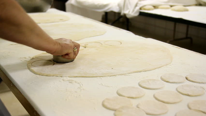 A woman uses a cookie cutter to cut circular shapes in dough.