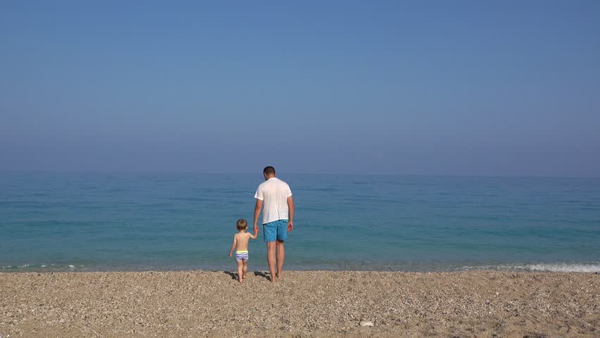 Father and little son stepping in the turquoise sea water