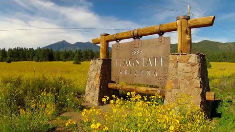 Wide angle shot of a Flagstaff Arizona sign. An old fashioned, Old West, Southwestern style sign is seen along the road, positioned in front of a view of Mount Humphrey.