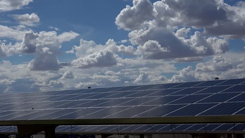 Time Lapse, Puffy white clouds sweep above rows of shiny, newly installed solar panels, bright blue sky. 4K UHD 3840x2160