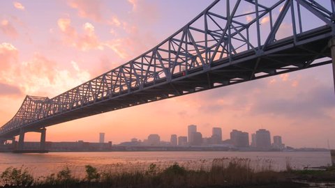 Time lapse of New Orleans skyline during sunset with Mississippi River and bridge in foreground.