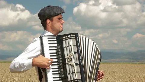 A man is playing the accordion amid a wheat field. 