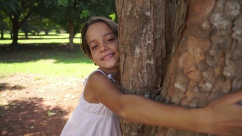 Ecology and environment, portrait of young caucasian girl embracing and hugging tree in park, happy child smiling and looking at camera. 9of18