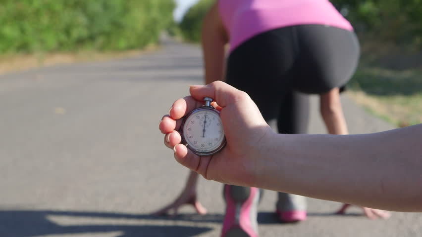 Personal fitness coach with stopwatch in hand timing female runner on road
