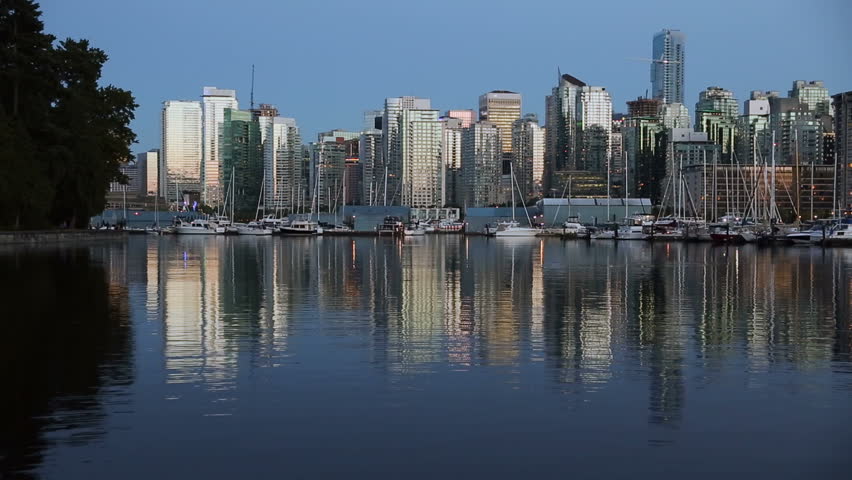Twilight Downtown Vancouver, Coal Harbor. Downtown Vancouver skyline at sunset looking across Coal Harbor from Stanley Park, British Columbia, Canada. Seagulls catch fish at the surface.