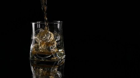 Whiskey being poured into a glass against black background. Long shot.  Slow motion