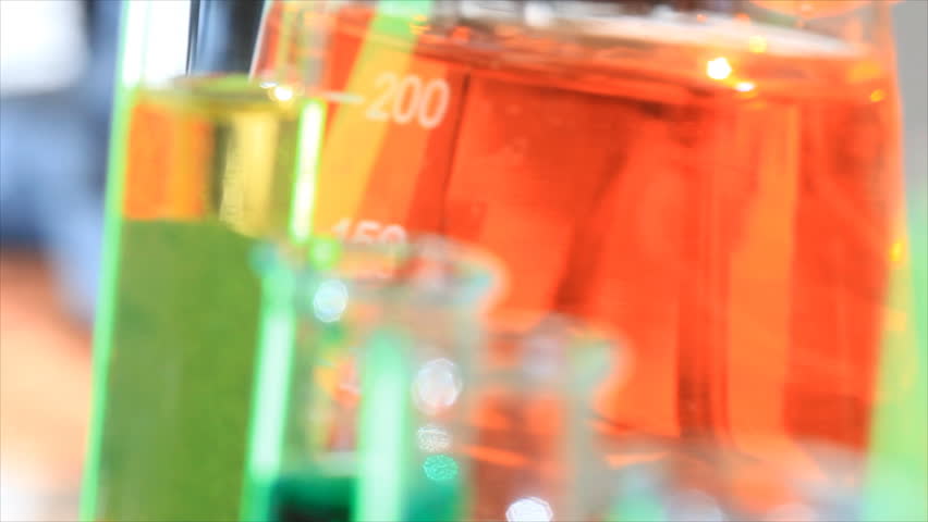Out of focus test tubes in the foreground with a flask filled with a colorful substance swirling in the background.