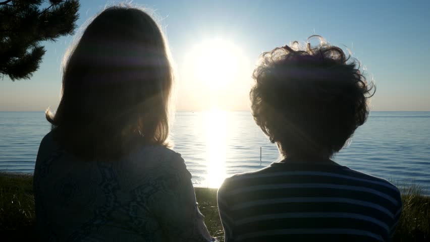 A Woman and an Elderly Woman Watch the Sunset Over a Lake. 4K