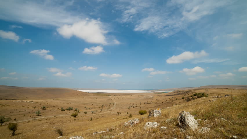 Clouds float over the fields and dry lake. Timelapse.