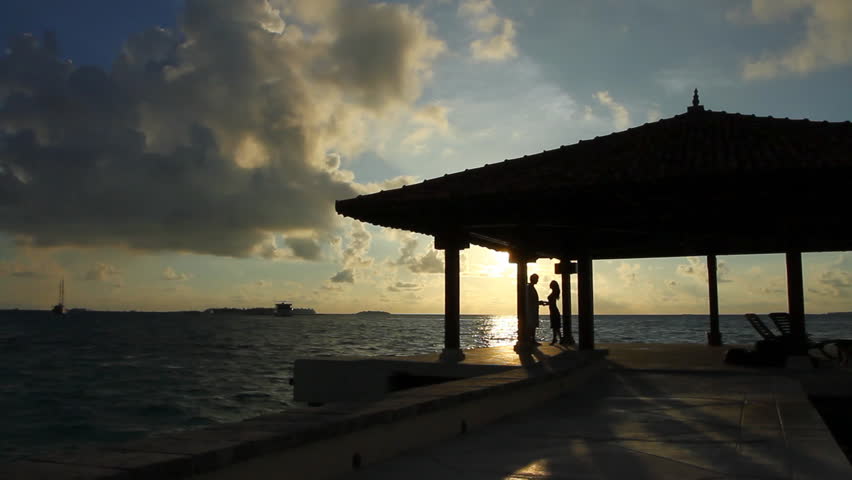 Romantic couple sitting next to palm tree at sunset 