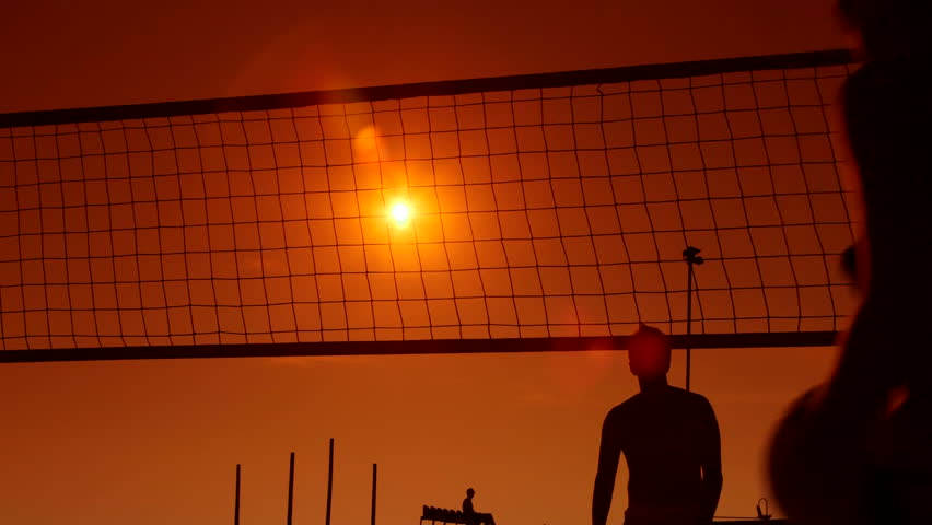 People enjoy playing volleyball on beach at sunset
