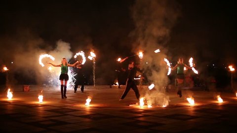 Boys spin pois and girls dance with burning fans at evening fireshow.