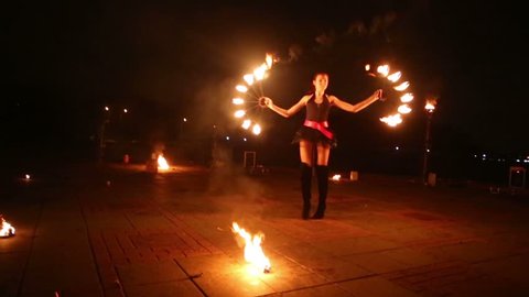 Young girl dances with burning torches shaped as fans at fire show in evening.