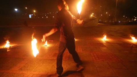 Boy dances and juggles burning pois at evening fire show.